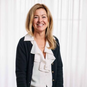 Carina noren sittandes på en stol i vit blus och kavaj