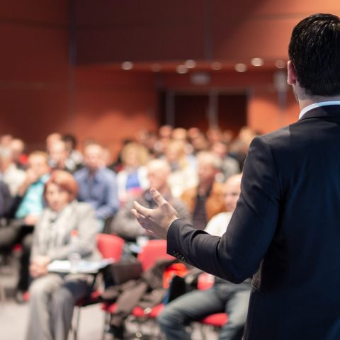 Speaker giving a talk on corporate business conference. Unrecognizable people in audience at conference hall. Business and Entrepreneurship event.