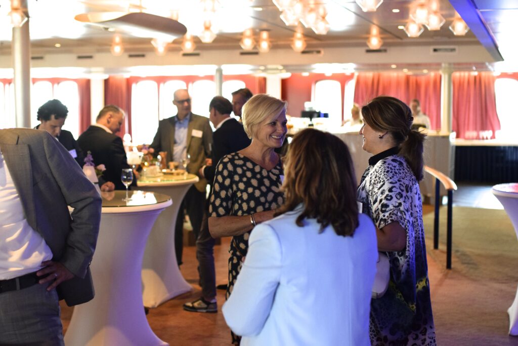 Netwerk event - zakelijke leiders staan in groepjes bij elkaar aan statafels en netwerken met elkaar.