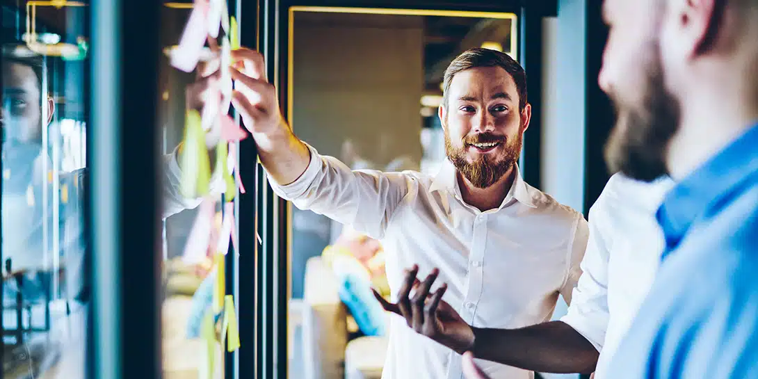 En gruppe mænd står og snakker foran en glasvæg med post-it notes