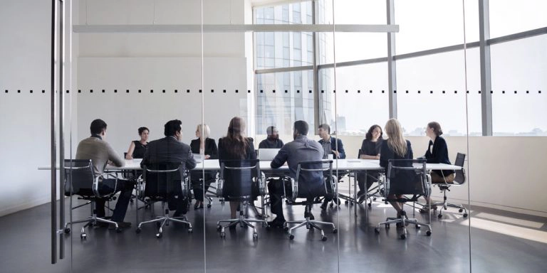 En gruppe mennesker sidder rundt om et bord bag en glasvæg