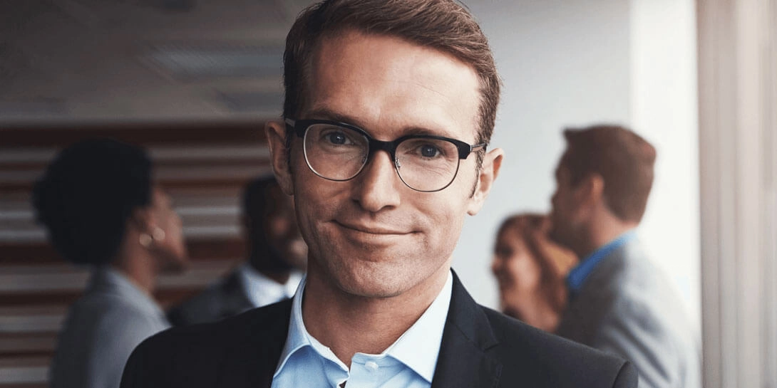 En mand i jakkesæt og med briller står foran en gruppe mennesker