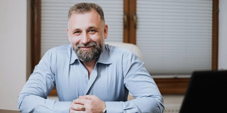 En mand med skæg i en blå skjorte sidder og smiler