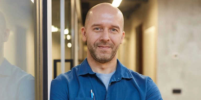 En skaldet mand med en blå skjorte og en kuglepen i lommen